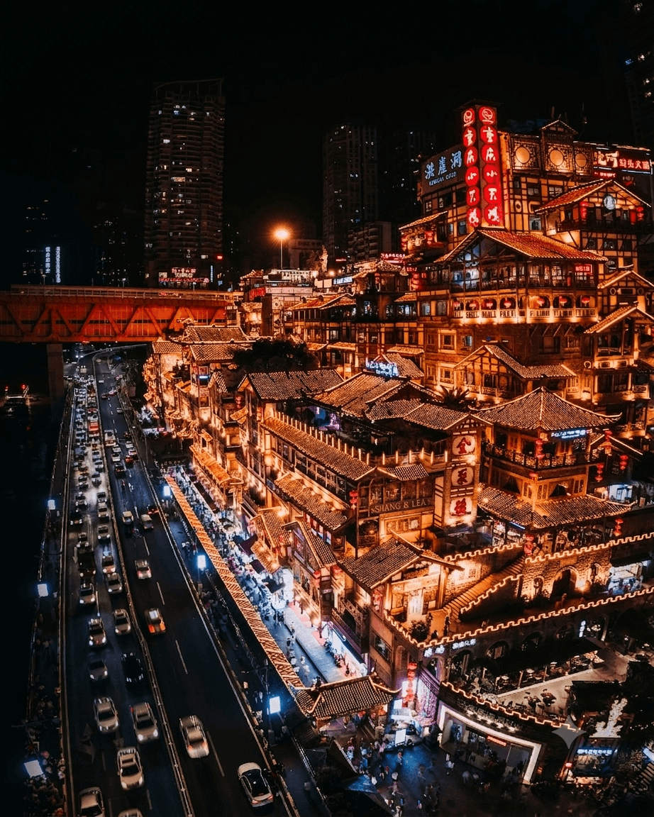 Hongya Cave in Chongqing at night: tiers of stilted pavilions glowing gold above a busy riverside road